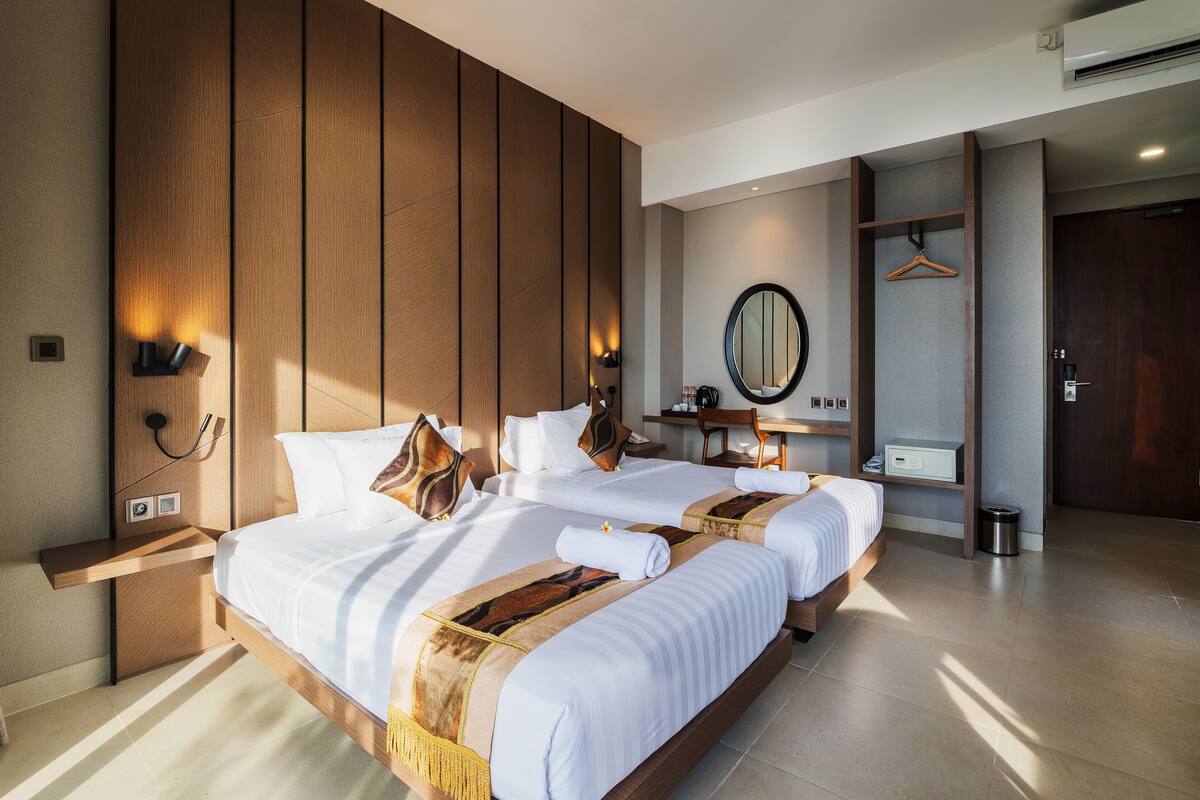A modern hotel room with a large bed, wooden paneling, a mirror, and a small desk.