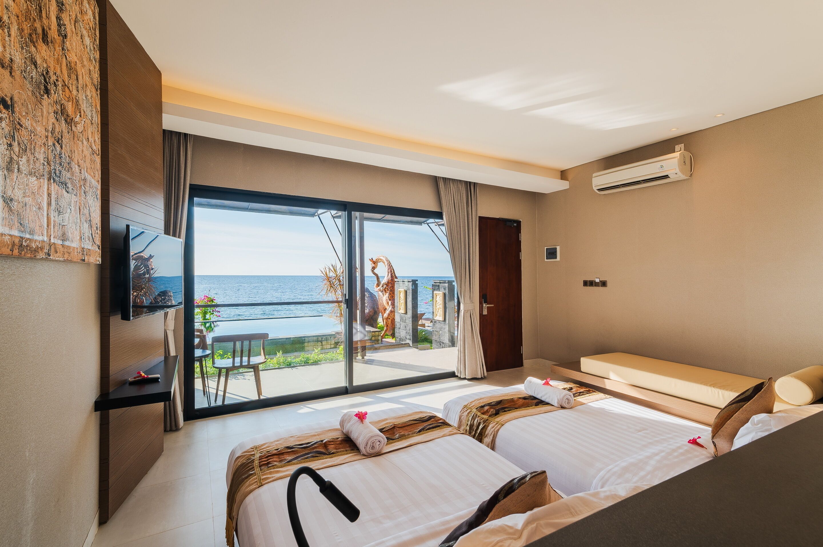 A hotel room with two beds, a TV, and a balcony with a view of the sea.