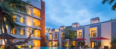 A modern hotel with a swimming pool, multiple balconies, and outdoor seating areas.