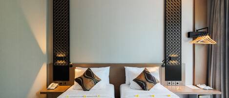 Habitación de hotel con dos camas, una mesita de noche con teléfono, un escritorio pequeño con radio y un perchero en la pared.