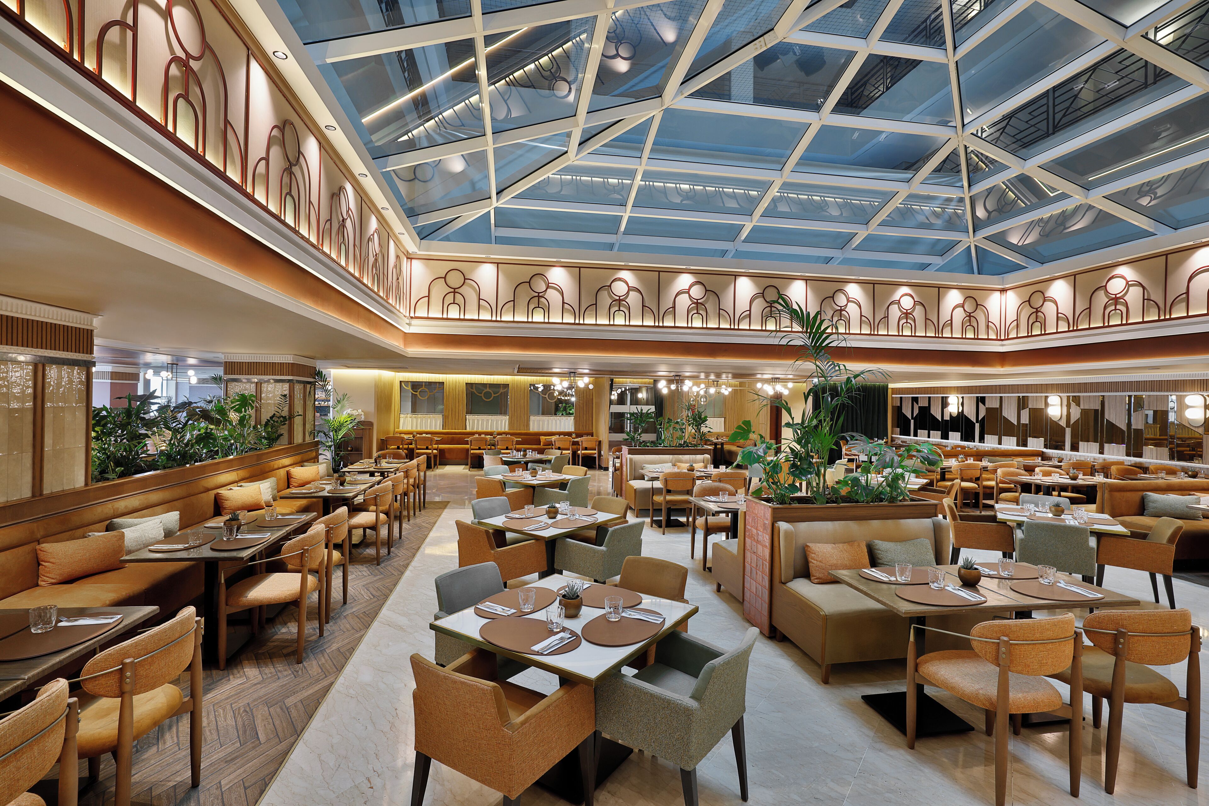 En rymlig hotellobby med flera matplatser, en central innergård med ett glastak och olika sittgrupper.