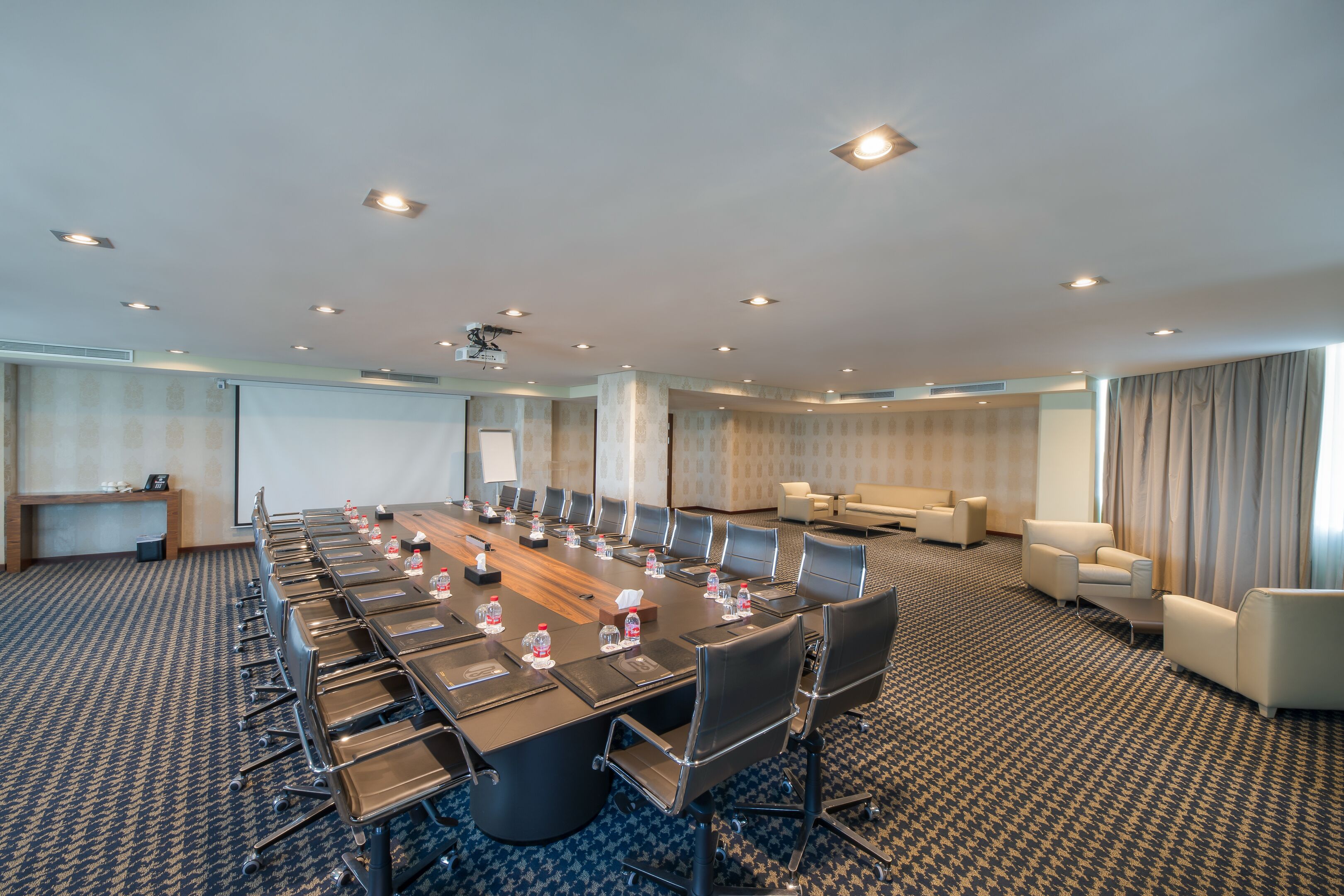 A conference room with a long table, multiple chairs, water bottles, and a projector screen.