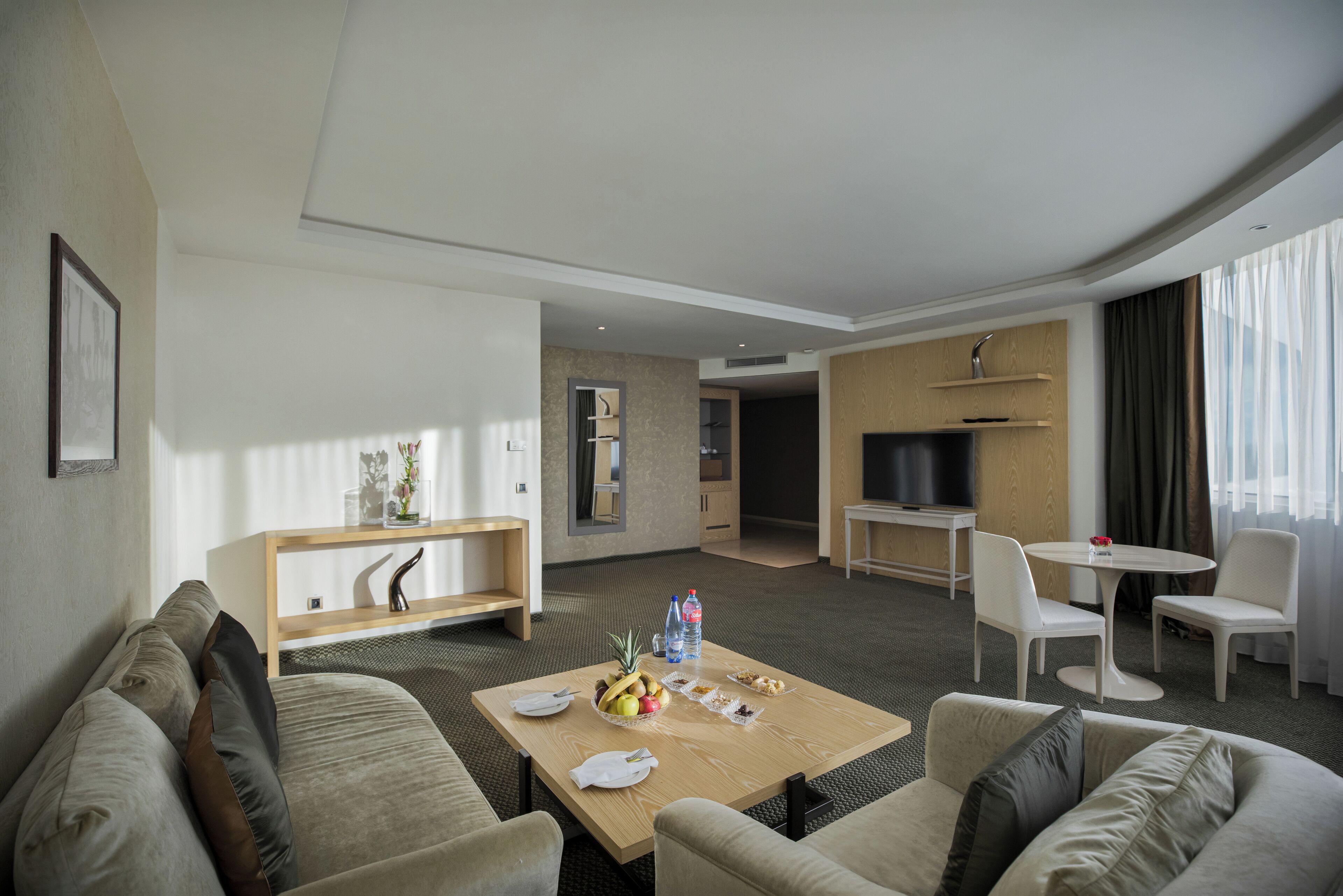 Una habitación de hotel moderna con sala de estar, mesa de comedor y televisor.