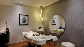 A spa room with a massage table, a large mirror, and a small vanity area.