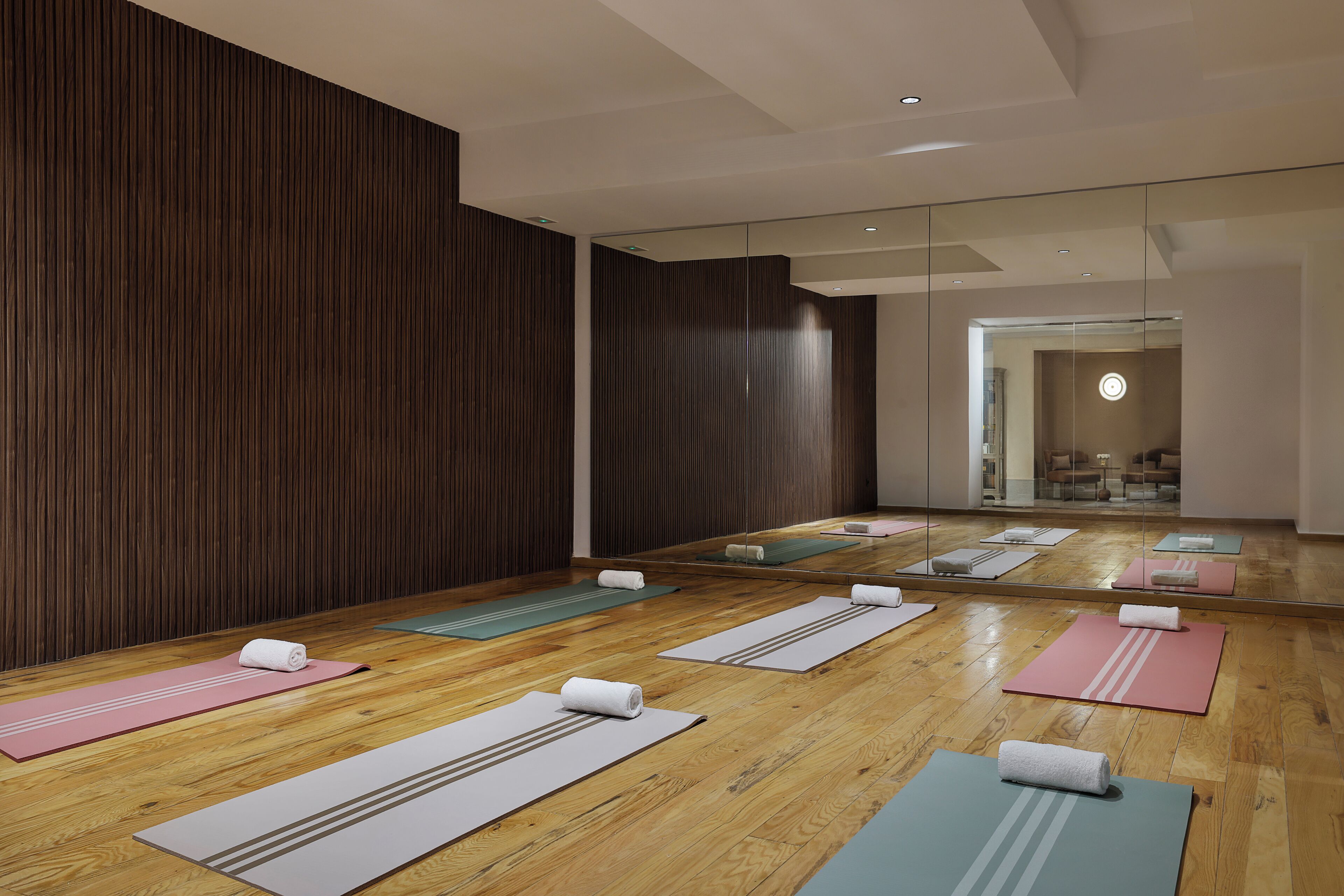Une pièce dotée d’un plancher en bois, de murs recouverts de miroirs et de plusieurs tapis de yoga disposés pour être utilisés.