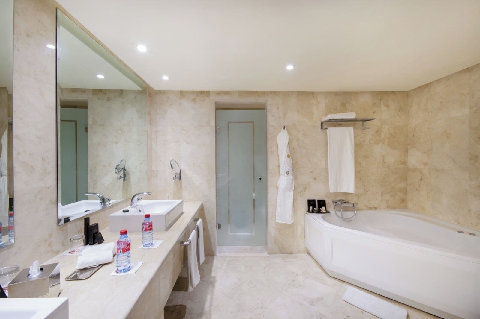 A modern bathroom with two sinks, a large mirror, a bathtub, and a shower area.