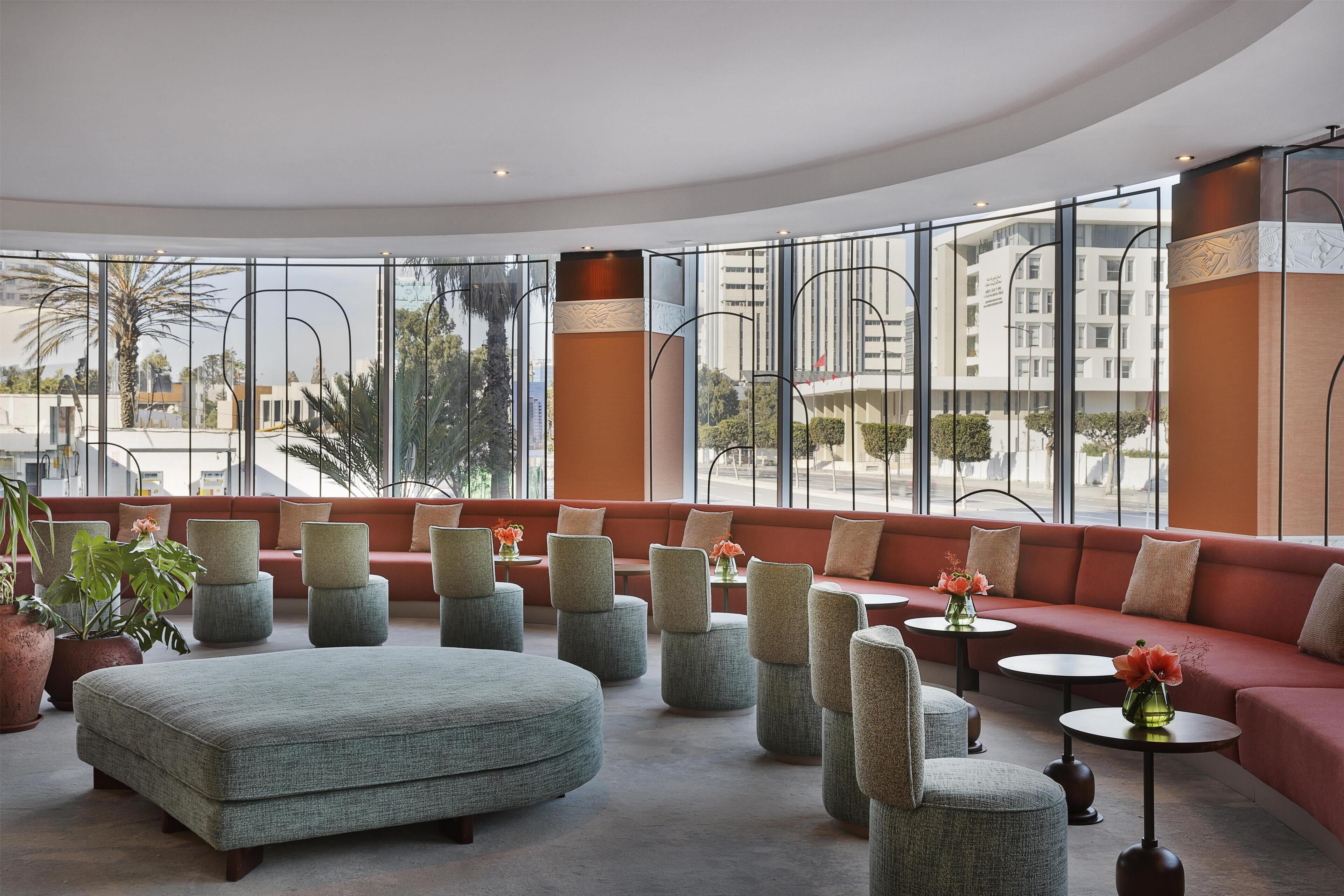 A modern lounge area with a curved seating arrangement, large windows offering a view of the city, and a mix of sofas and ottomans.