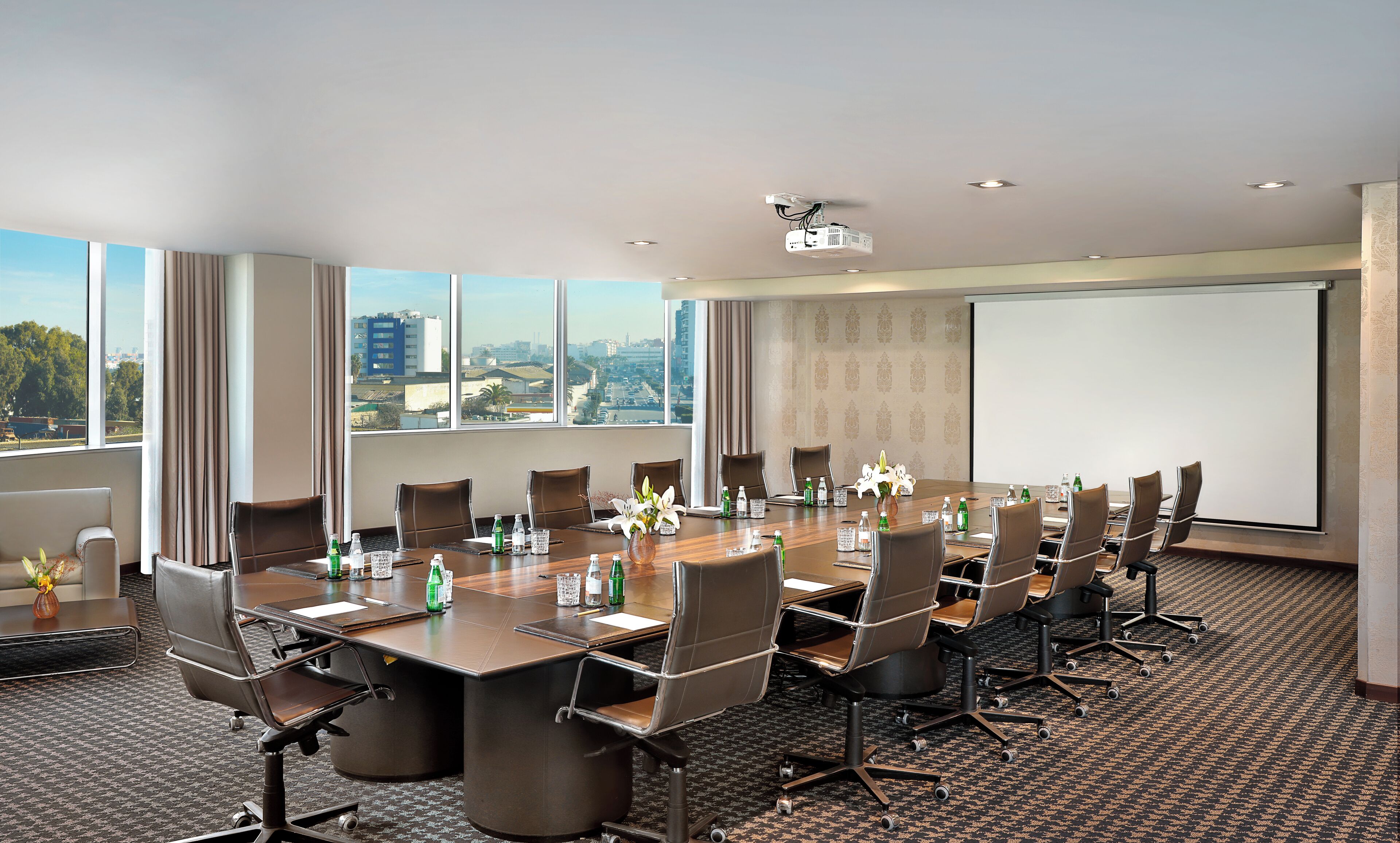 Ein Konferenzraum mit großem Tisch, Stühlen, einem Projektor und Blick auf die Stadt durch große Fenster.
