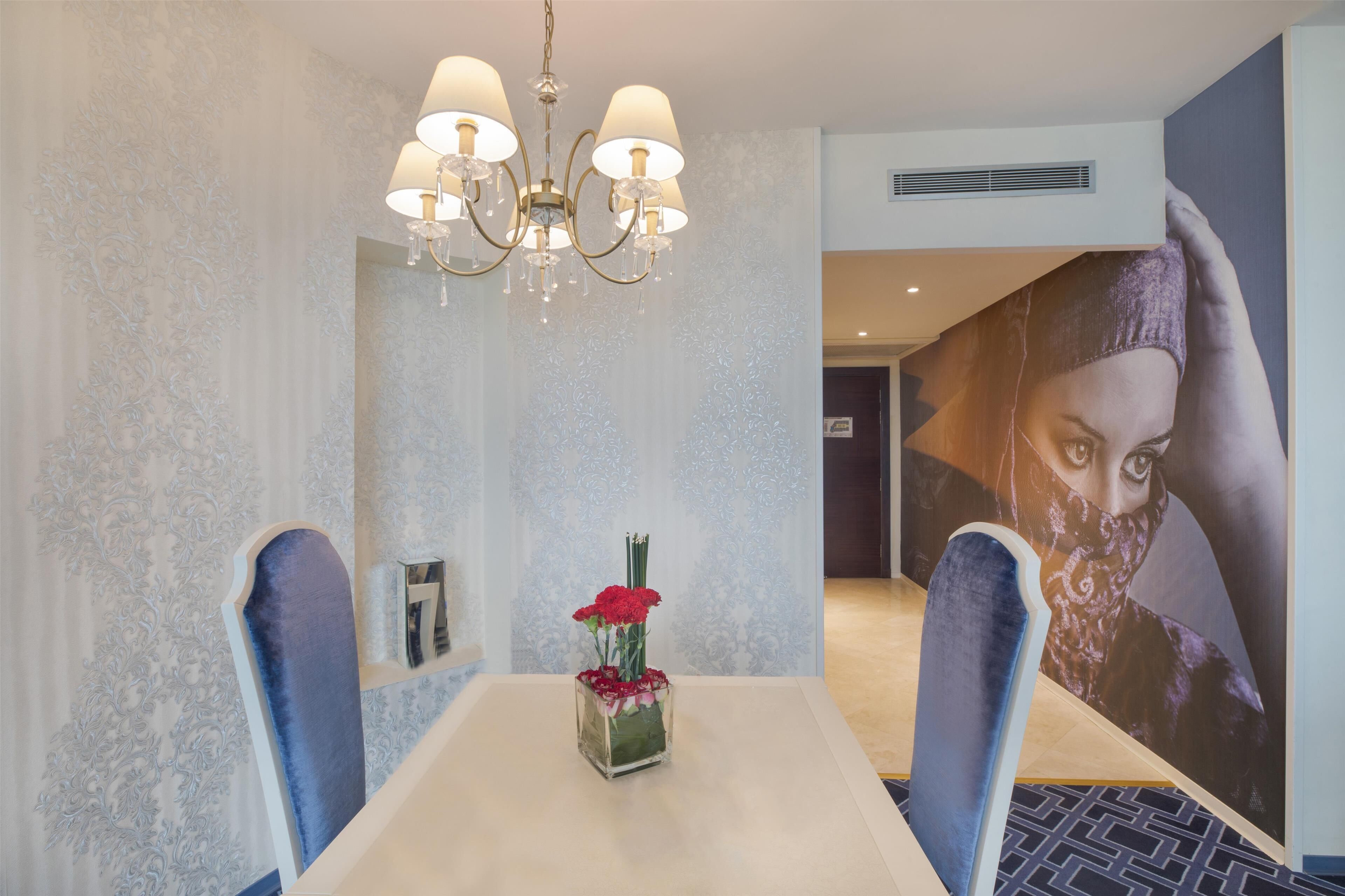A dining area with a chandelier, a vase with red flowers, and a large poster on the wall.