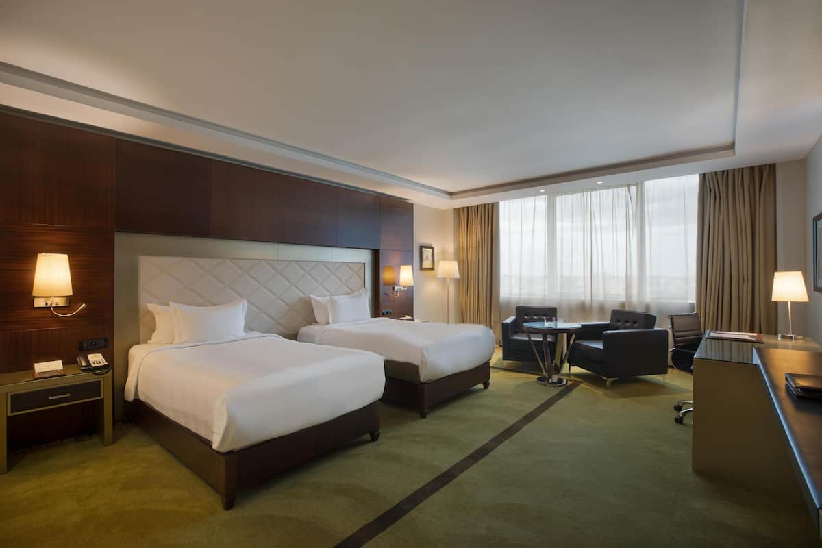 Une chambre d’hôtel avec deux lits, un bureau, une chaise, un téléphone et une fenêtre avec des rideaux.