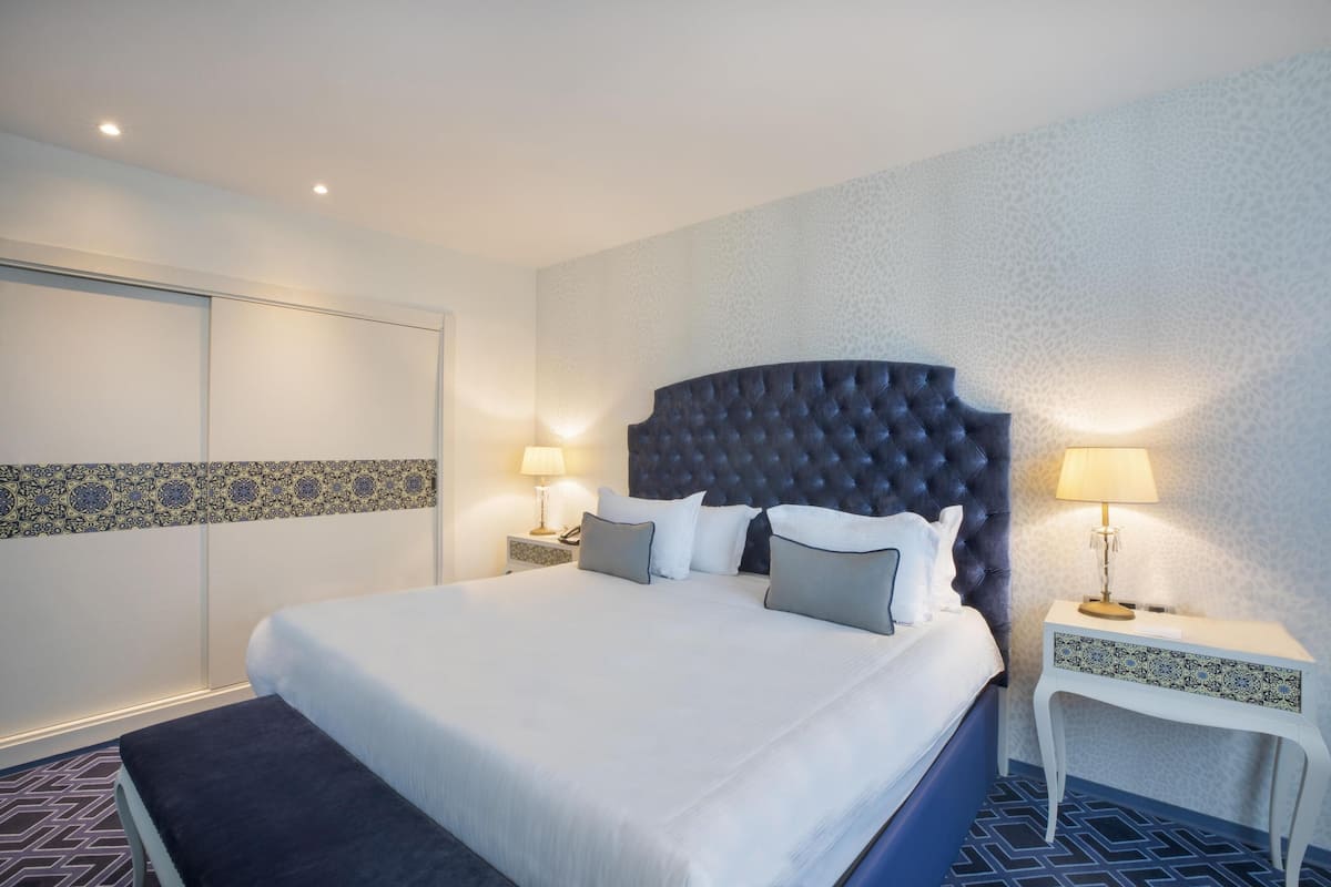 Une chambre d’hôtel avec un grand lit, deux tables de chevet avec des lampes, un mur à motifs et une moquette bleue.
