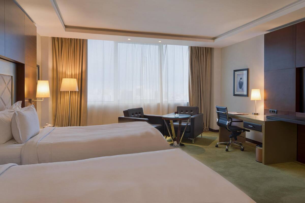 Une chambre d’hôtel avec deux lits, un bureau, une chaise, une télévision et une fenêtre avec des rideaux.