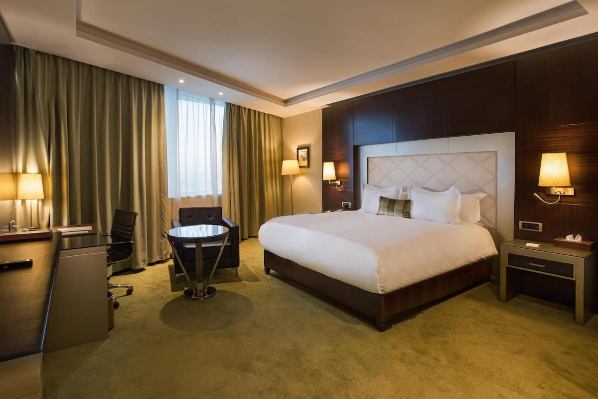 Une chambre d’hôtel avec un grand lit, un bureau avec une chaise, une petite table et deux lampes de chevet.