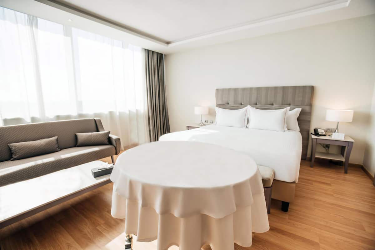 Une chambre d’hôtel avec un lit, un canapé, une table ronde et une table de chevet avec des lampes.