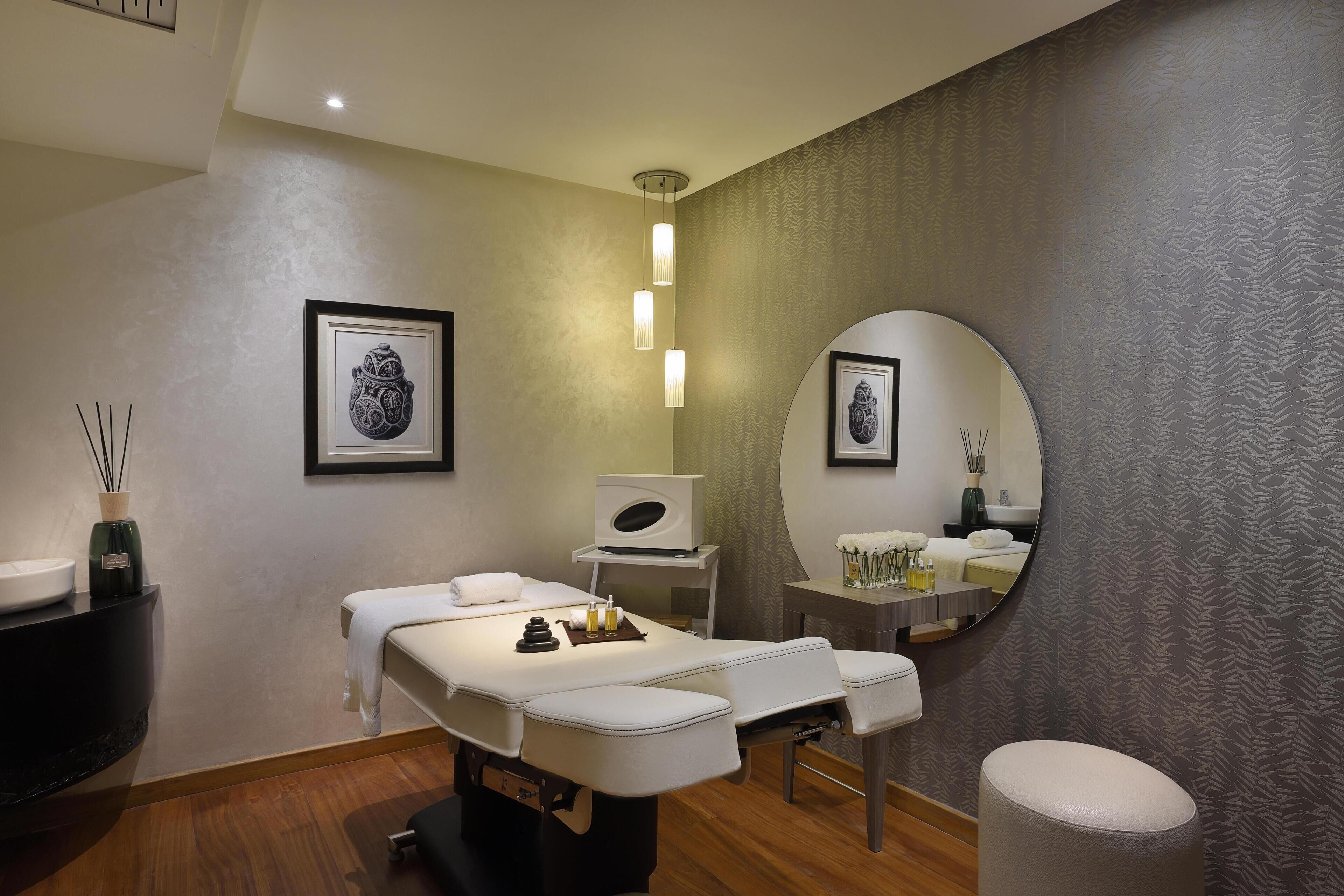 A modern spa room with a massage table, a large mirror, and a sink.