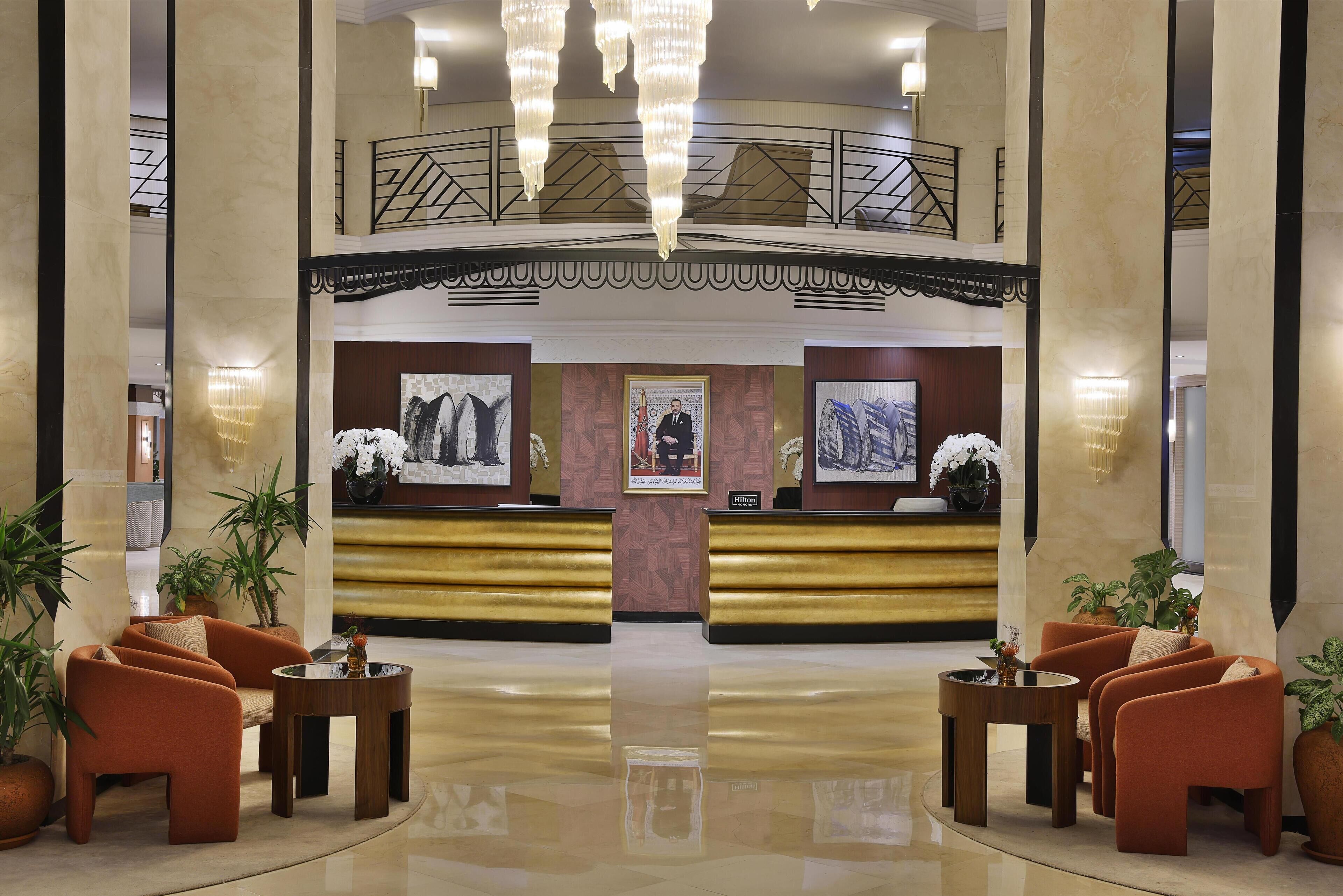 A hotel lobby with a reception desk, seating area, and a staircase.