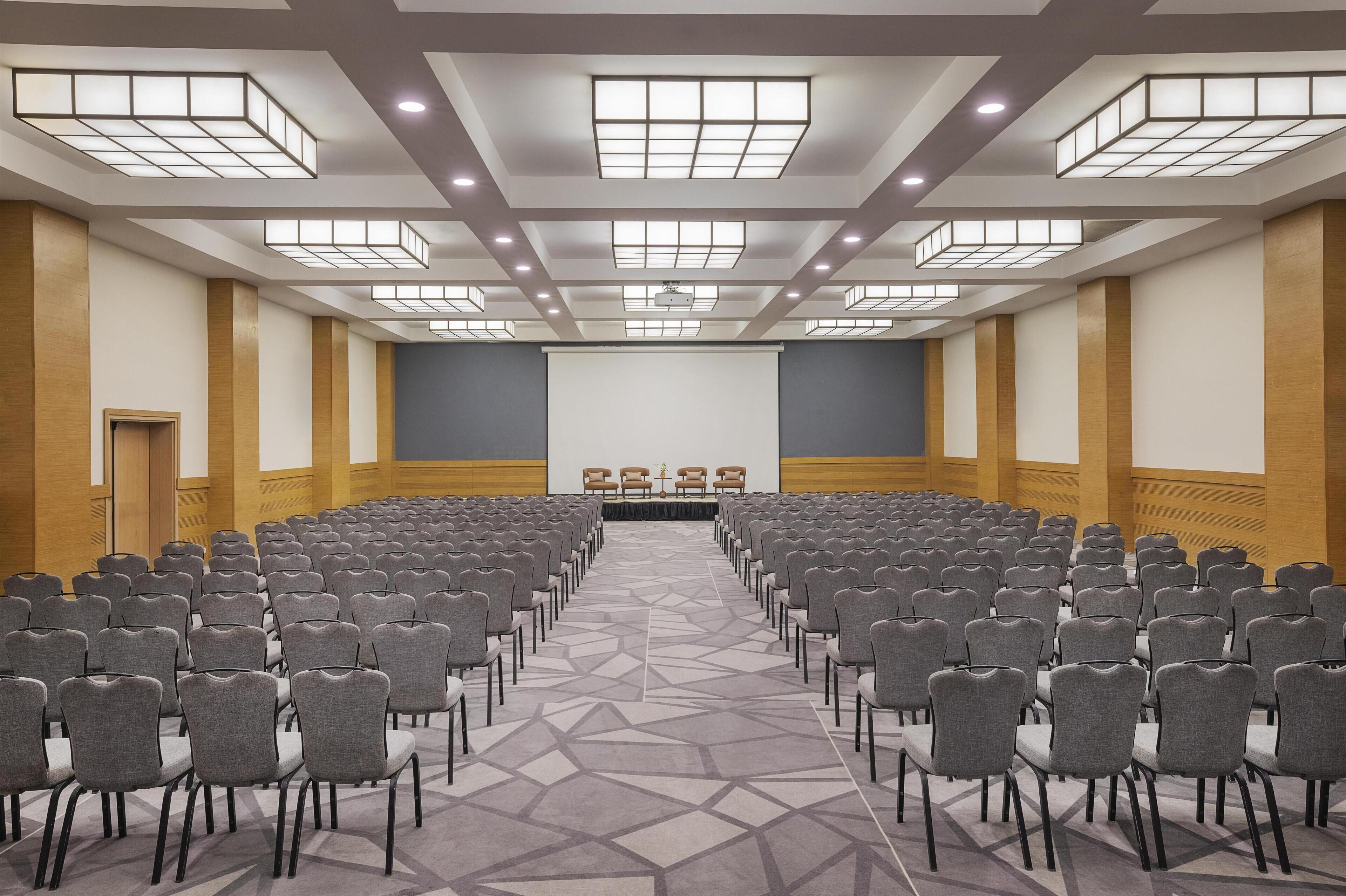A conference room with rows of chairs facing a stage with a projector screen.
