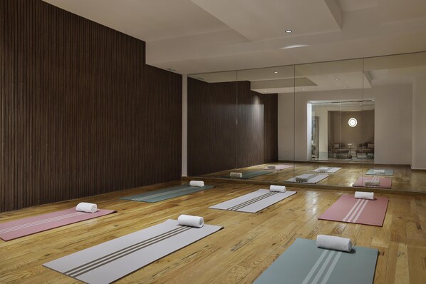 A spacious room with wooden flooring, multiple yoga mats, and a large mirror reflecting the room.