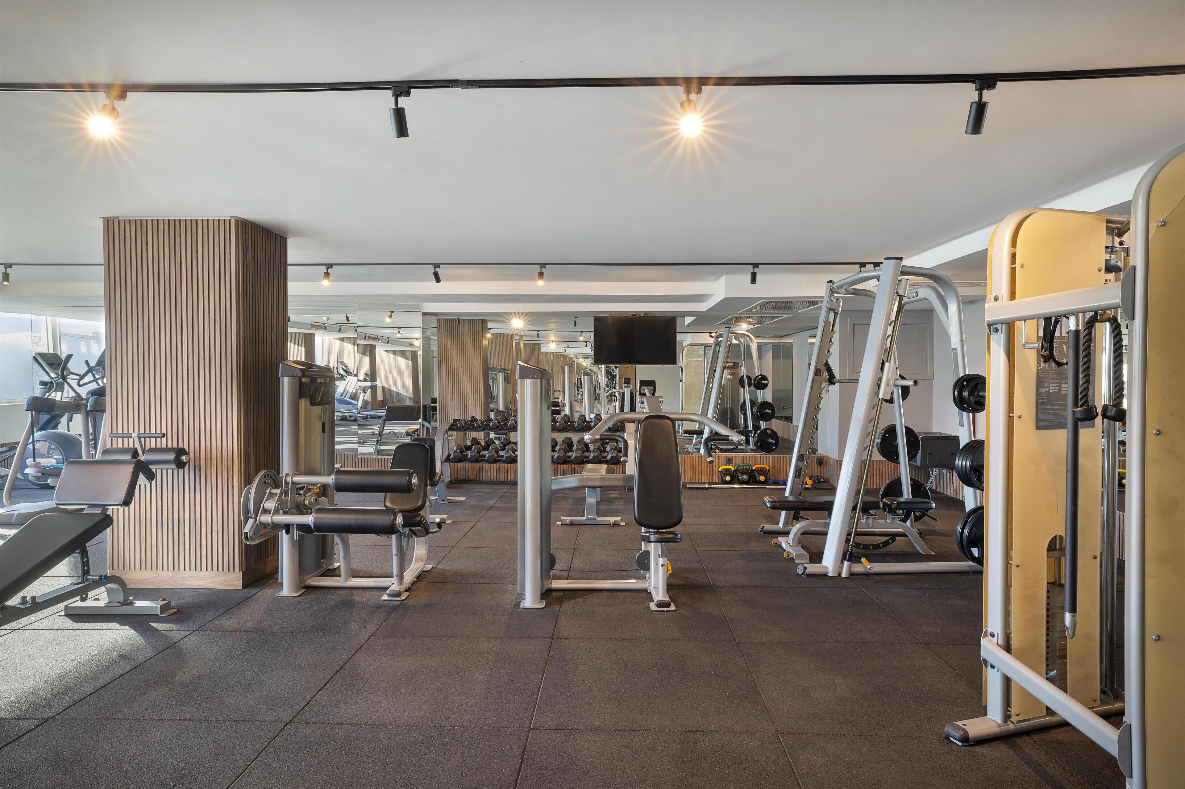 Un gimnasio con diversos equipos de ejercicio, que incluye máquinas de pesas y pesas libres, dispuesto en un espacio amplio.