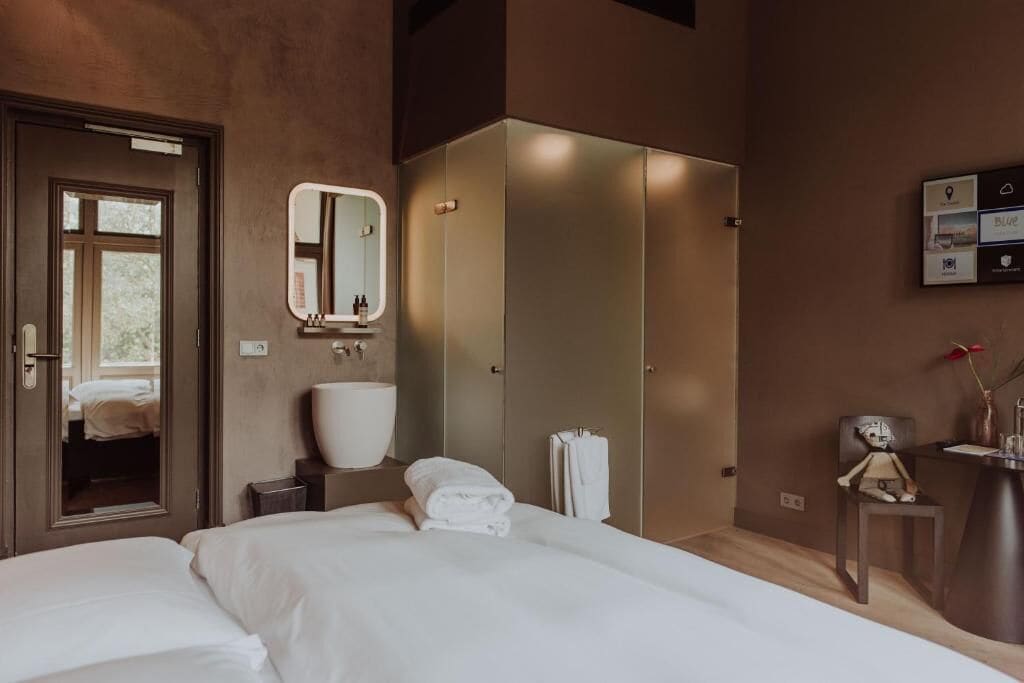 Una habitación de hotel moderna con una cama grande, un baño con espejo, un armario y una pequeña mesa con un florero.