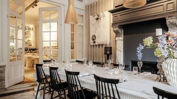 Comedor con una mesa larga dispuesta para una comida, flanqueada por sillas negras, y una zona de bar visible a través de un arco.