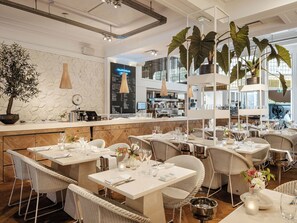 A restaurant interior with high tables, wicker chairs, and hanging plants. - Boutique Hotels MANNA & Blue (Nijmegen)