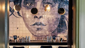 A bar area with a large mural, bar stools, and a variety of bottles and glasses.