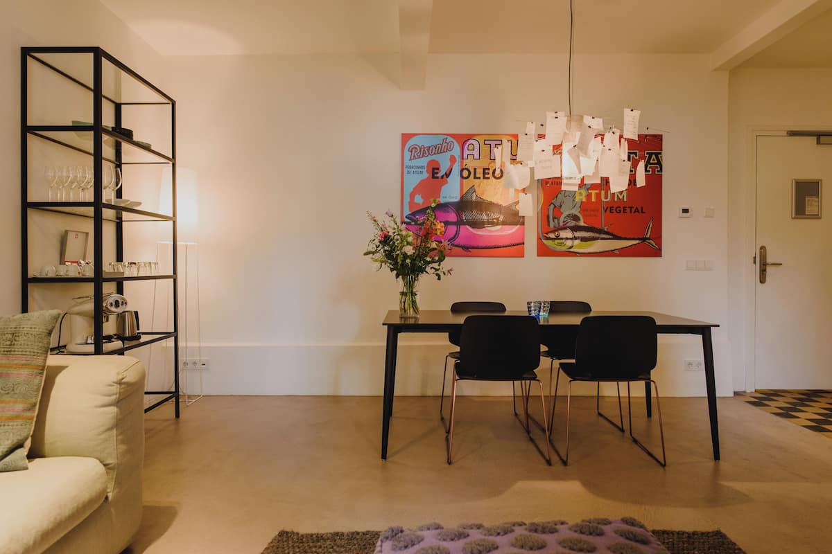 Un comedor con una mesa, sillas, una estantería y una pared decorada con carteles.