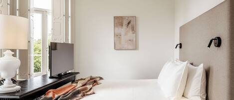 A hotel room with a bed, a desk with a lamp, a television, and a painting on the wall.