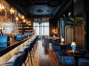 A bar area with a long counter, blue upholstered chairs, and a wooden floor. - Boutique Hotels MANNA & Blue (Nijmegen)