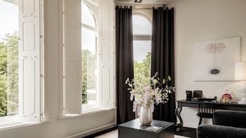 A room with a large window, a black coffee table, a chair, and a painting on the wall.