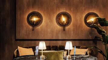 Een zithoek met een bank, twee bijzettafels met lampen, en een grote wandlamp.