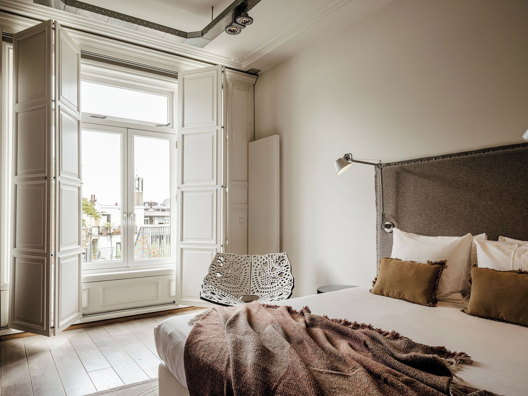 Ein Hotelzimmer mit Bett, Schreibtisch, Stuhl, Fenster mit Blick auf Gebäude und einer Deckenleuchte.