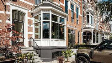 Een rij herenhuisachtige woningen met erkers, een bord met de naam van een boetiekhotel, en een geparkeerde SUV.