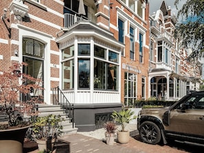 A row of traditional brick townhouses with bay windows, a boutique hotel sign, and a parked SUV. - Boutique Hotels MANNA & Blue (Nijmegen)