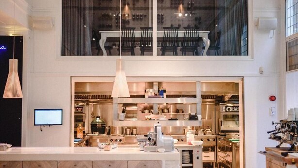 A modern kitchen with stainless steel appliances, a large island, and a view of the dining area through a large window. - Boutique Hotels MANNA & Blue (Nijmegen)