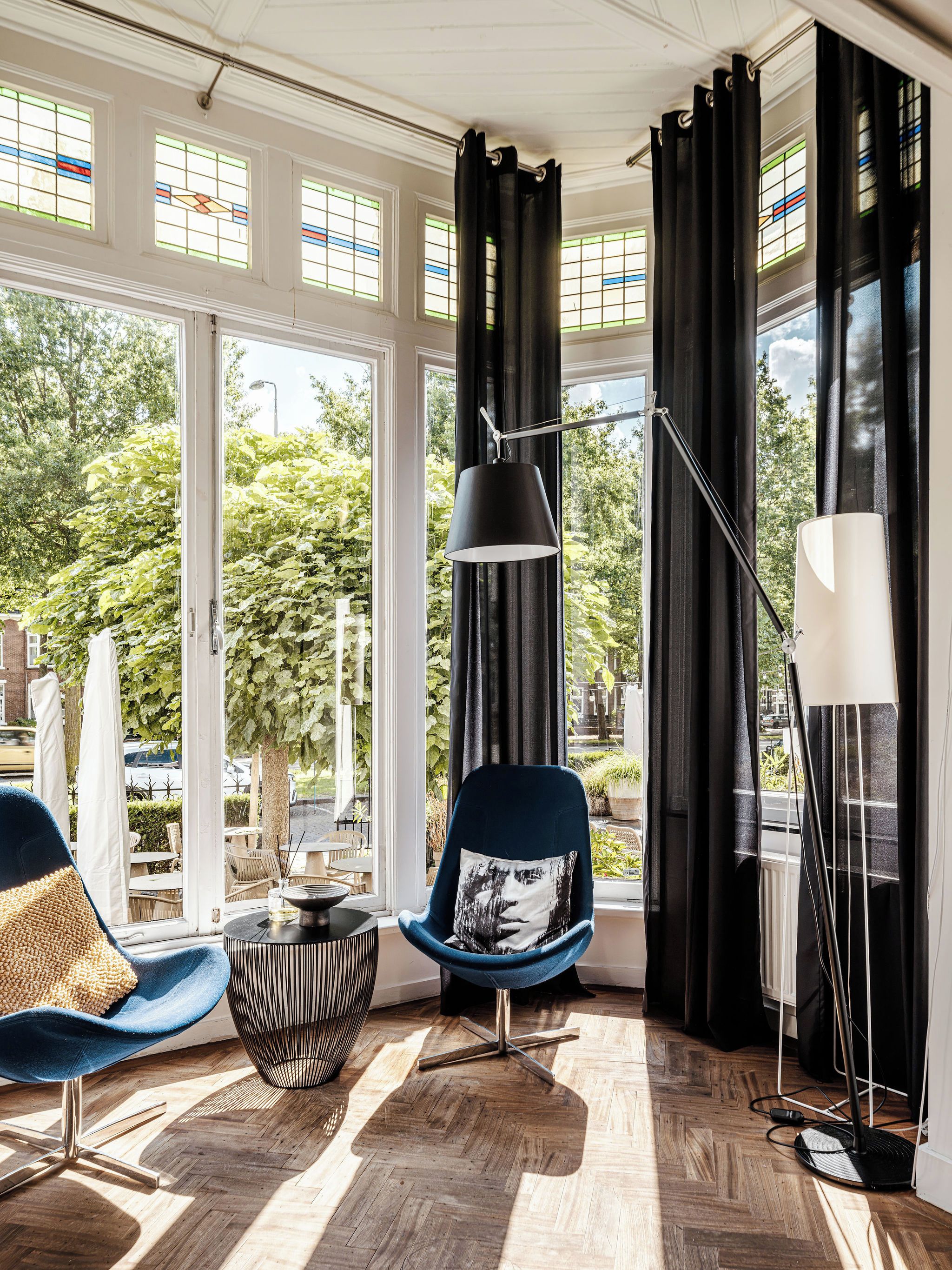 A modern room with a large window, a blue chair with a cushion, a floor lamp, and a table with a candle.