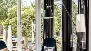 Une chambre moderne avec une grande fenêtre, un fauteuil bleu avec un coussin, un lampadaire et une table sur laquelle est posée une bougie.