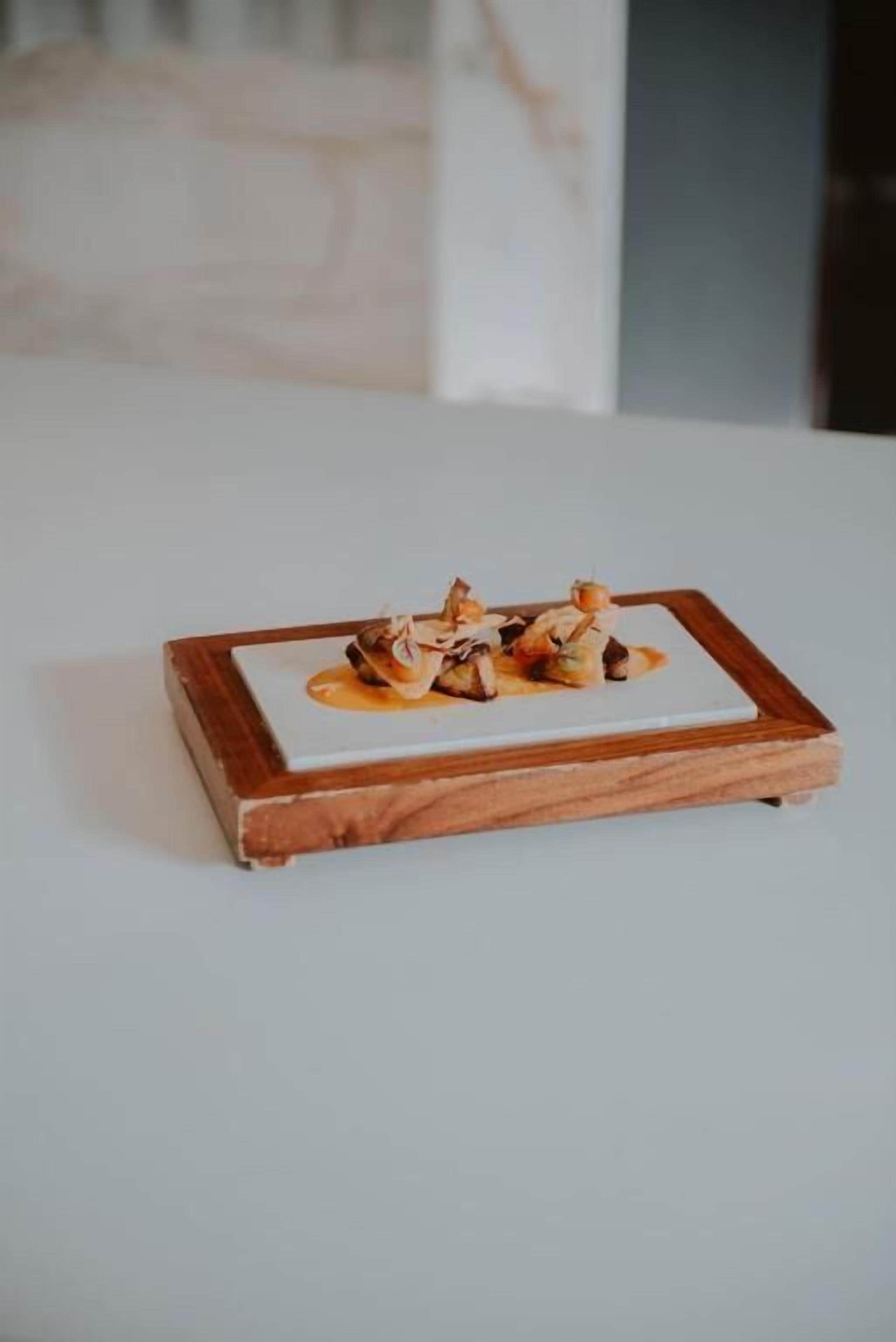 A square wooden table with a white surface, holding a dish of food.