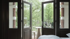 An open door leading to a balcony with a view of trees and a brick building. - Boutique Hotels MANNA & Blue (Nijmegen)