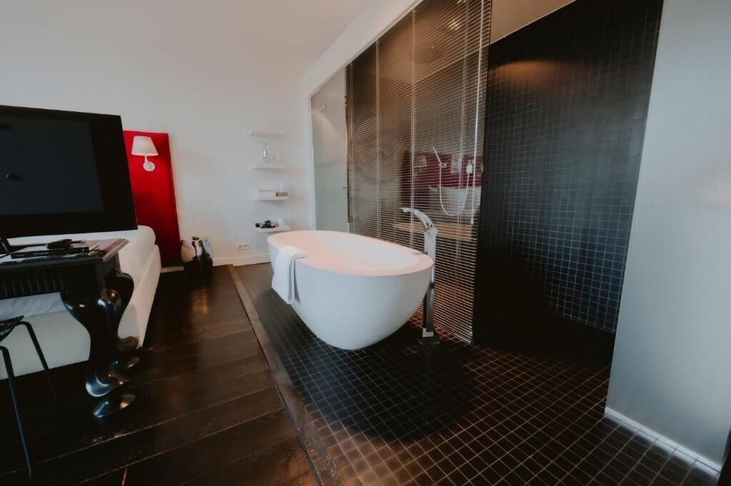 Une salle de bain moderne avec une baignoire sur pieds, un meuble-lavabo avec un miroir et un mur d’accent de couleur rouge.