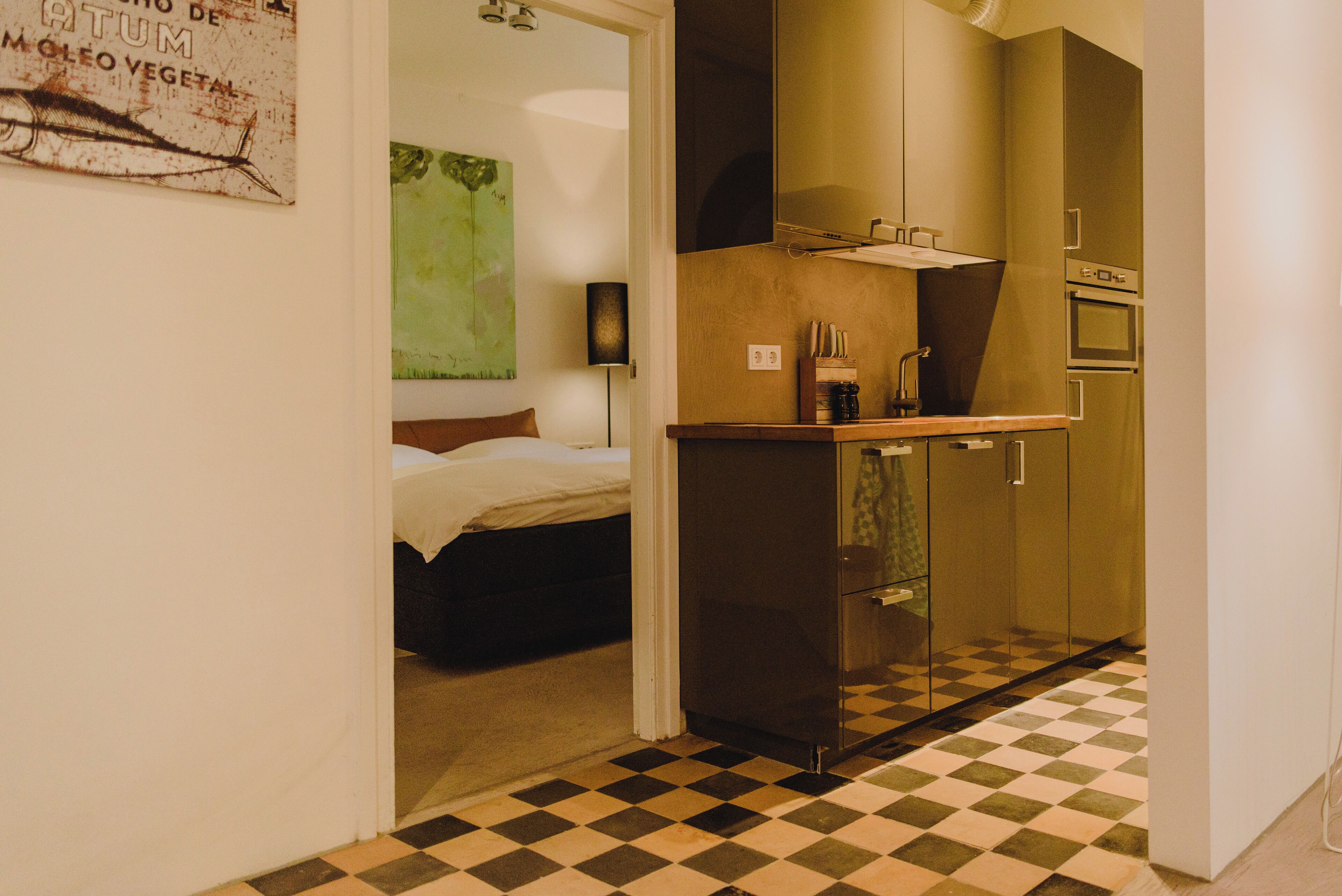 A compact hotel room with a bed, a small kitchenette, and a checkered floor.