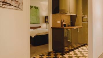 Een kleine hotelkamer met een bed, een kitchenette en een geruit vloertje.