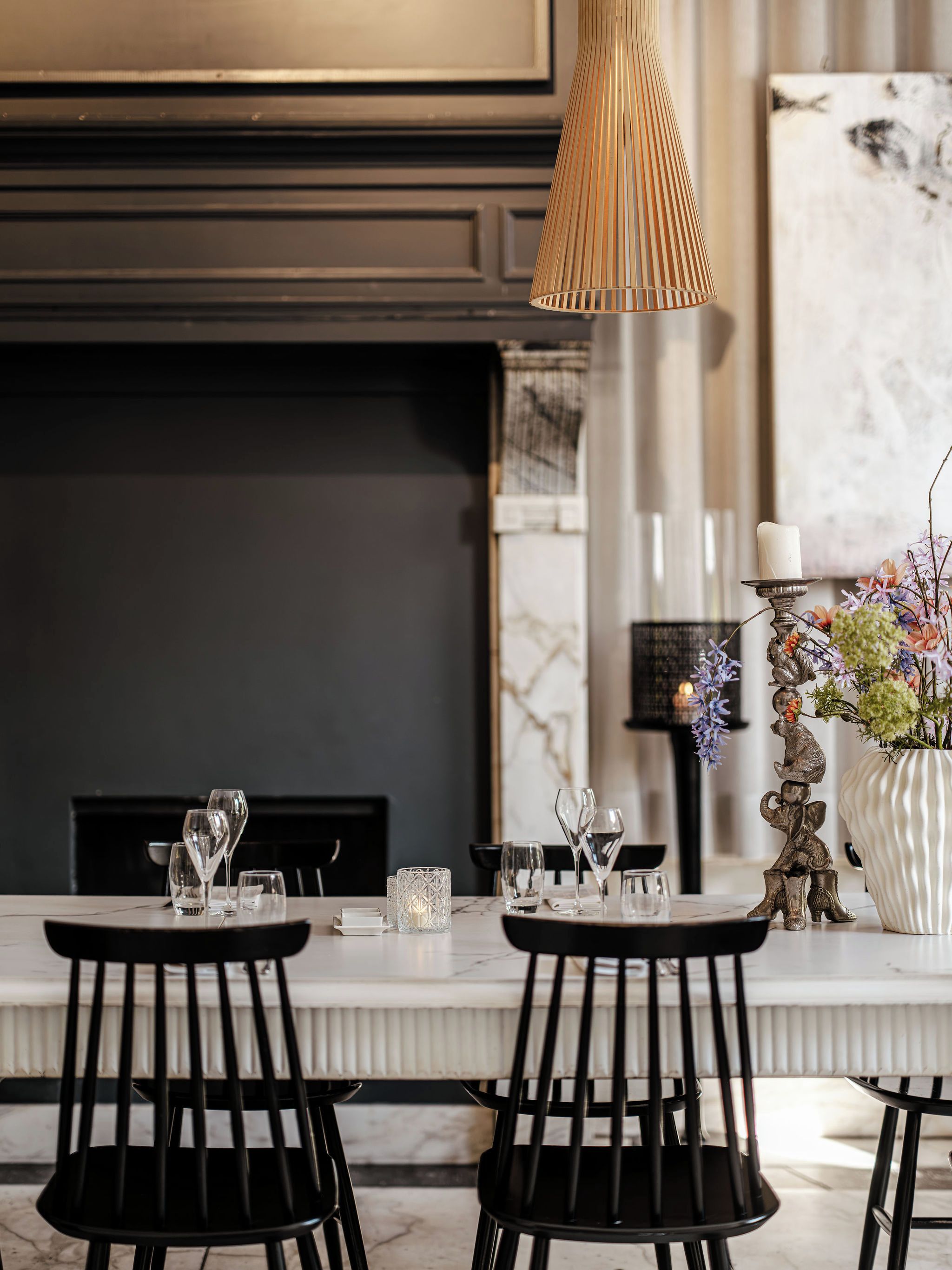 A dining area with a fireplace, a tall candle holder, and a vase with flowers.
