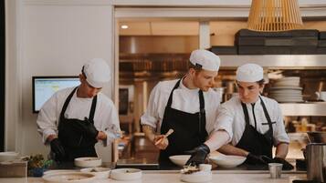Tres cocineros en una cocina moderna con electrodomésticos de acero inoxidable y una lámpara colgante de madera.