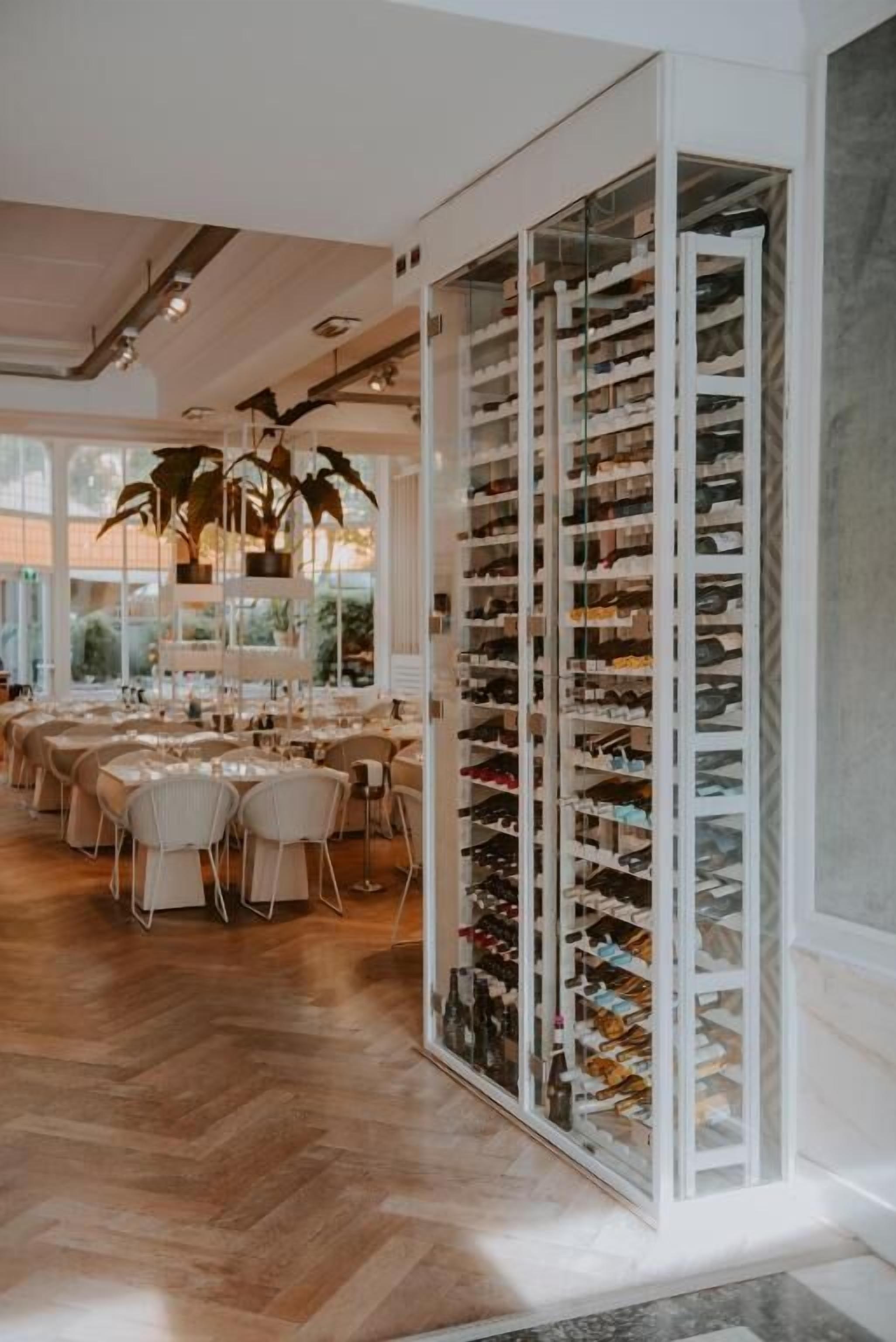 A restaurant with a long, open shelving unit filled with shoes, a wooden herringbone floor, and a dining area with tables and chairs.