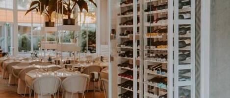 A restaurant with a long, open shelving unit filled with shoes, a wooden herringbone floor, and a dining area with tables and chairs.