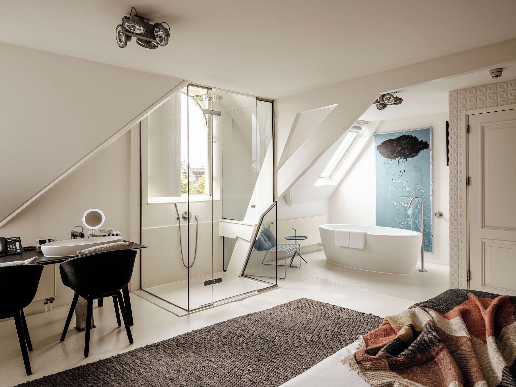 A modern bedroom with a glass shower enclosure, a large window, a desk with a mirror, and a bathtub.