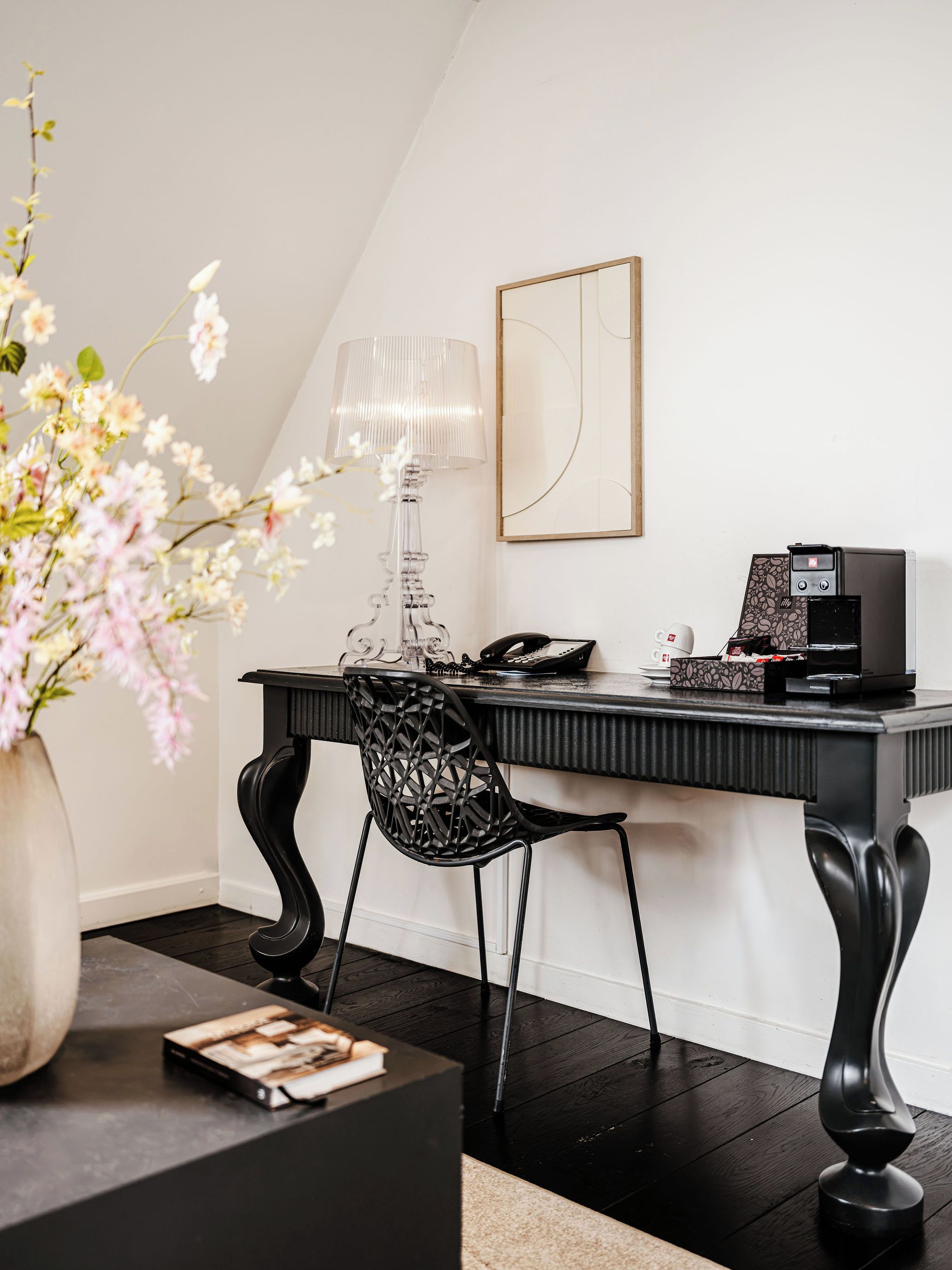 A modern office space with a desk, chair, coffee machine, and a vase with flowers.