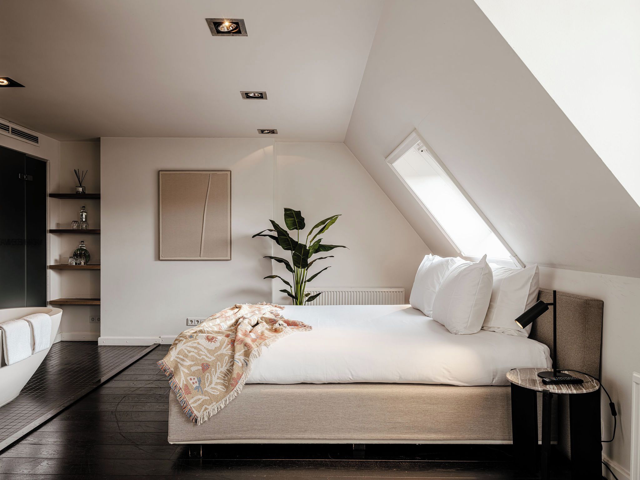 A modern bedroom with a bed, bedside table, lamp, and a large window.